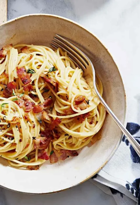 Martha Stewart bacon pasta with cheese sauce and thyme, spaghetti twirled in a bowl and topped with crisp bacon pieces