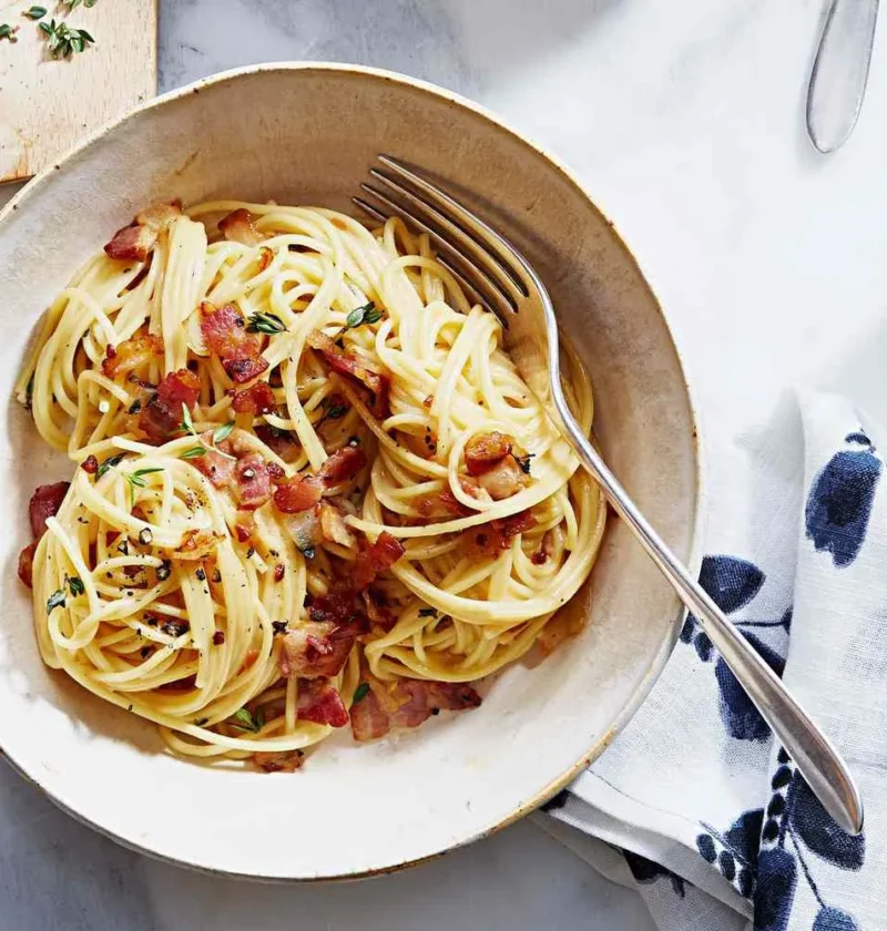 Martha Stewart bacon pasta with cheese sauce and thyme, spaghetti twirled in a bowl and topped with crisp bacon pieces