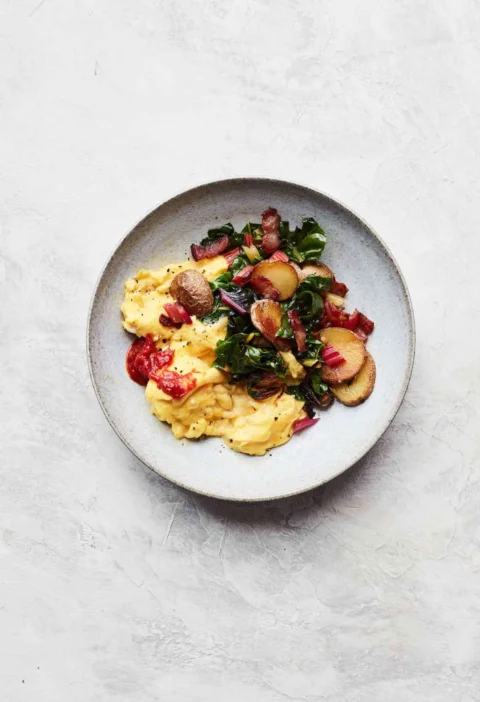 Martha Stewart bacon, potato, and Swiss chard scramble with soft scrambled eggs, sliced potatoes and chard on a gray plate