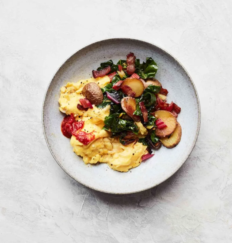 Martha Stewart bacon, potato, and Swiss chard scramble with soft scrambled eggs, sliced potatoes and chard on a gray plate