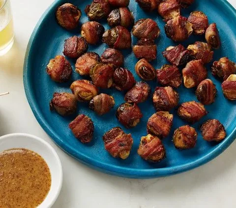 Martha Stewart bacon-wrapped brussels sprouts on a blue platter with toothpicks and a bowl of grainy mustard dipping sauce