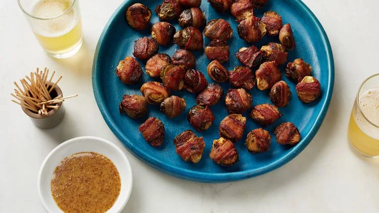 Martha Stewart bacon-wrapped brussels sprouts on a blue platter with toothpicks and a bowl of grainy mustard dipping sauce