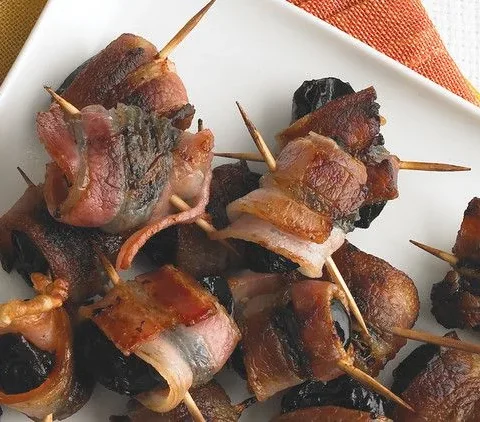 Martha Stewart bacon-wrapped prunes secured with toothpicks on a white plate, browned and crisp