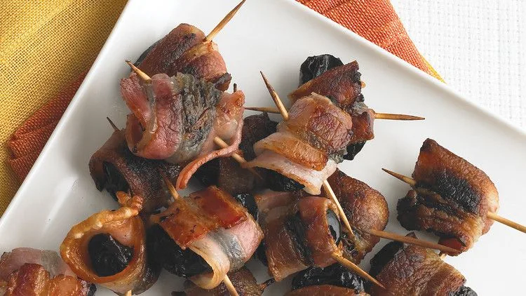 Martha Stewart bacon-wrapped prunes secured with toothpicks on a white plate, browned and crisp