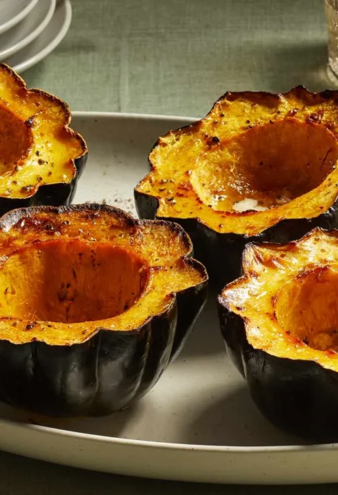 Four baked acorn squash halves with brown sugar and butter, caramelized and golden, served on a white oval platter