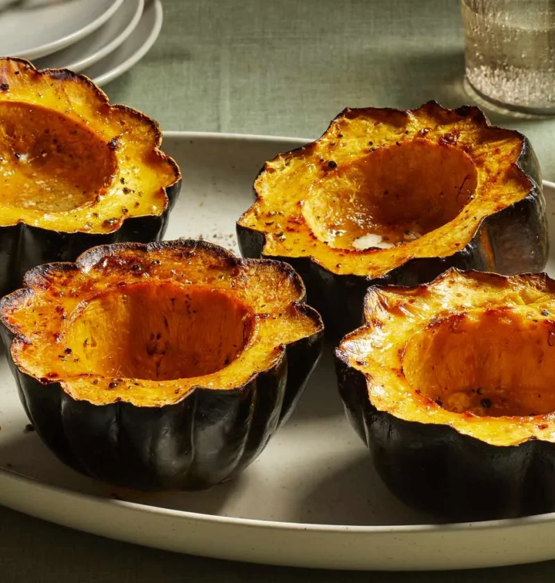 Four baked acorn squash halves with brown sugar and butter, caramelized and golden, served on a white oval platter