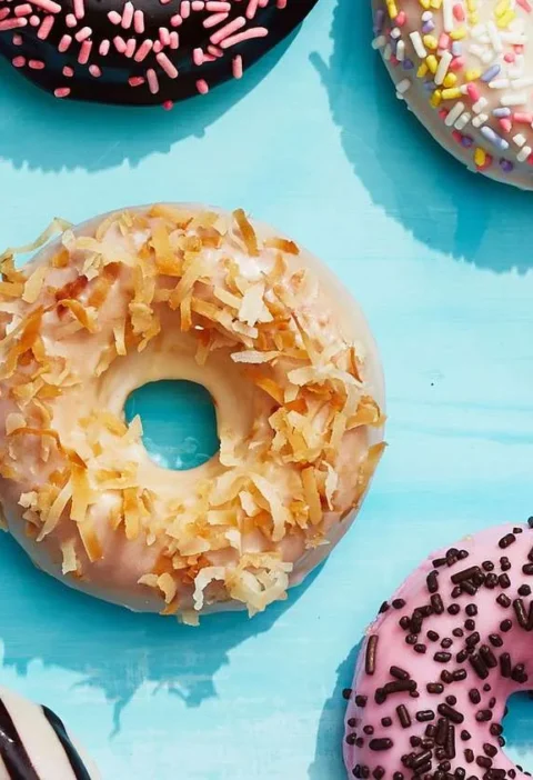 Martha Stewart baked cake donuts with pink sprinkle glaze, coconut flakes and chocolate sprinkles on a blue background