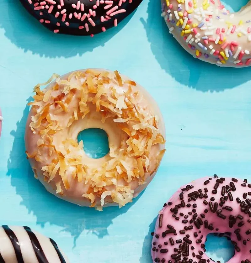Martha Stewart baked cake donuts with pink sprinkle glaze, coconut flakes and chocolate sprinkles on a blue background