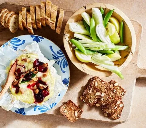 Martha Stewart baked Camembert with cherry jam and toasted nuts on a blue patterned plate beside fennel, green apple slices, crackers and baguette