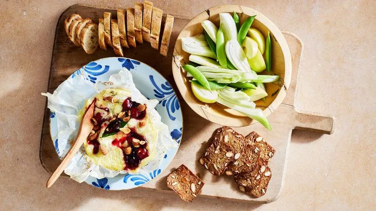 Martha Stewart baked Camembert with cherry jam and toasted nuts on a blue patterned plate beside fennel, green apple slices, crackers and baguette