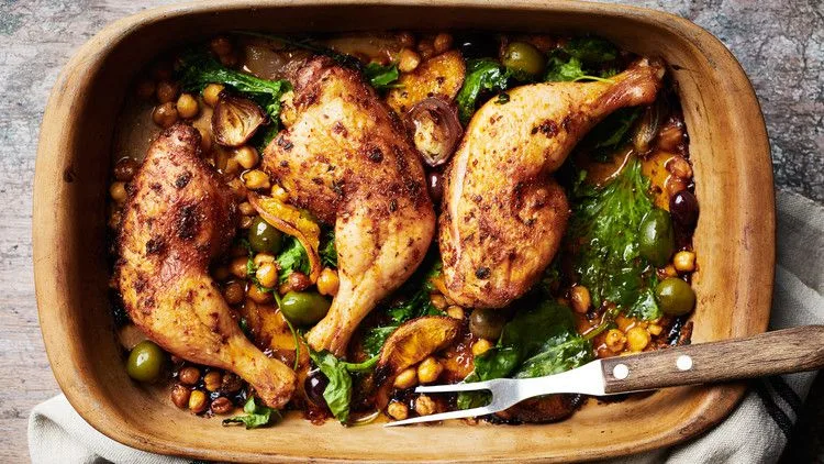 Martha Stewart baked chicken legs with chickpeas, olives and greens in a rustic baking dish with a serving fork