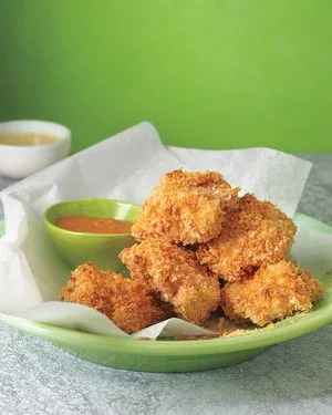 Martha Stewart baked chicken nuggets piled in a green bowl on parchment with two small dipping sauces