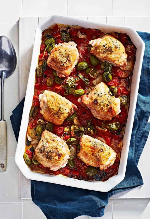 Martha Stewart baked chicken Veracruz with golden chicken thighs, green olives, tomatoes and shallots in a white baking dish