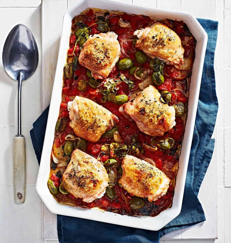 Martha Stewart baked chicken Veracruz with golden chicken thighs, green olives, tomatoes and shallots in a white baking dish