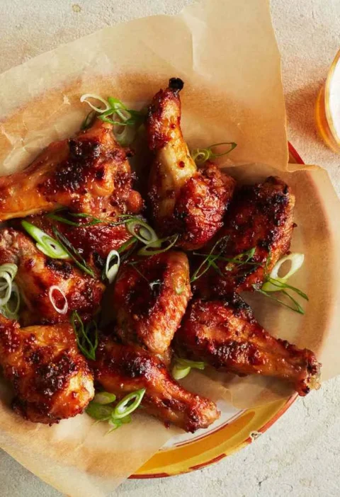 Martha Stewart baked chicken wings with mustard-marmalade glaze topped with sliced scallions on parchment paper next to a glass of beer