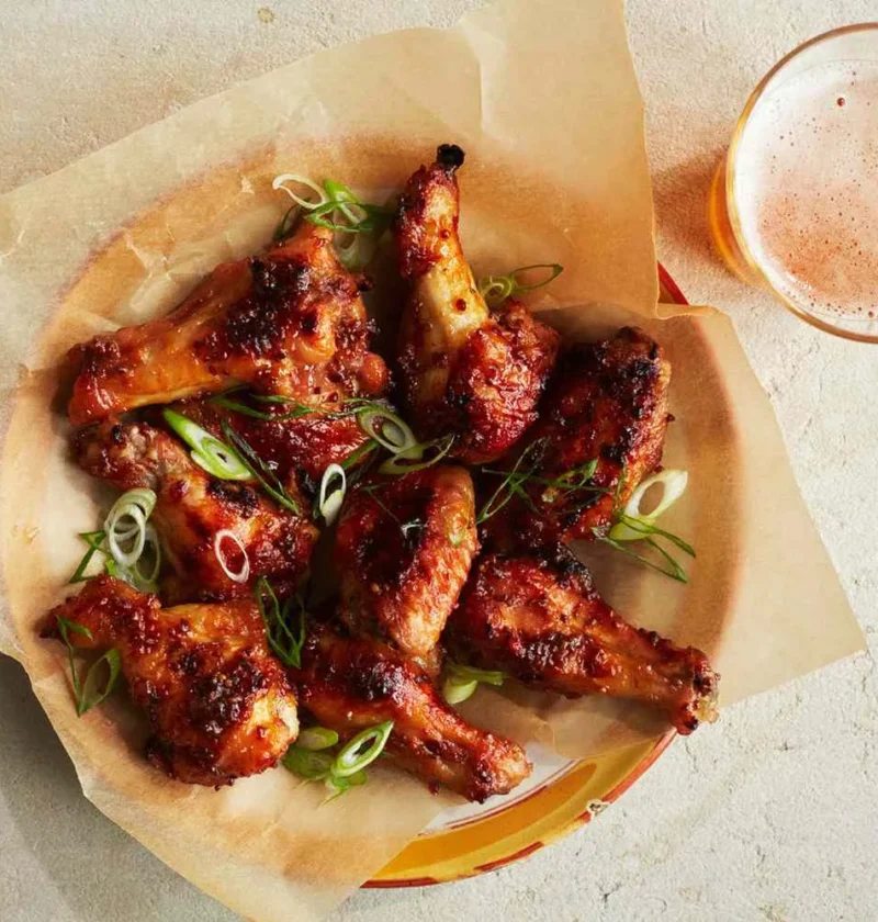 Martha Stewart baked chicken wings with mustard-marmalade glaze topped with sliced scallions on parchment paper next to a glass of beer