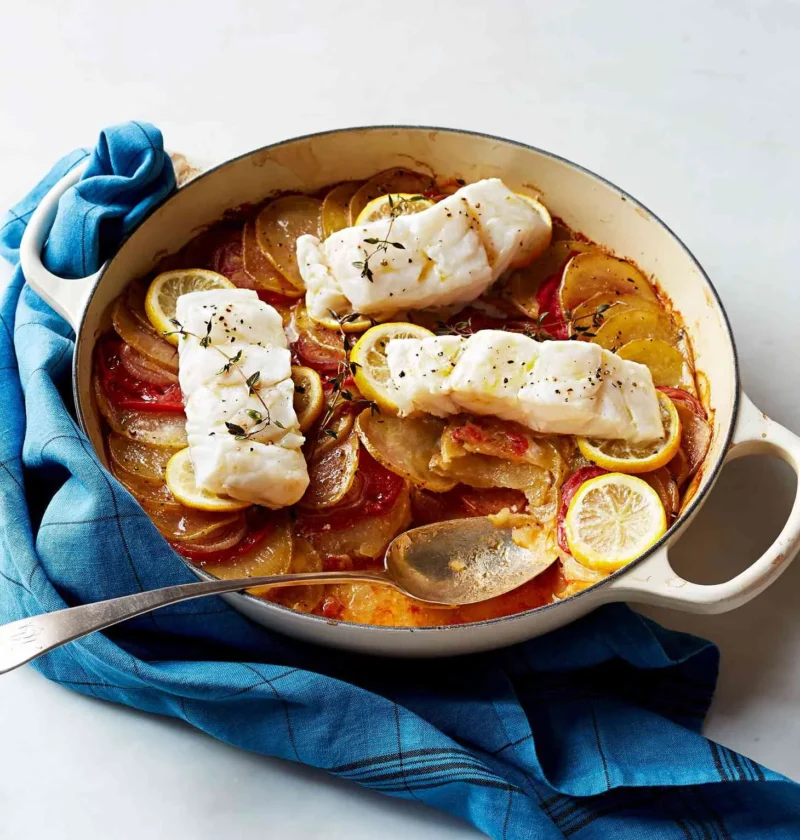 Martha Stewart baked cod with tomatoes and potatoes in a cream Dutch oven topped with lemon slices and thyme