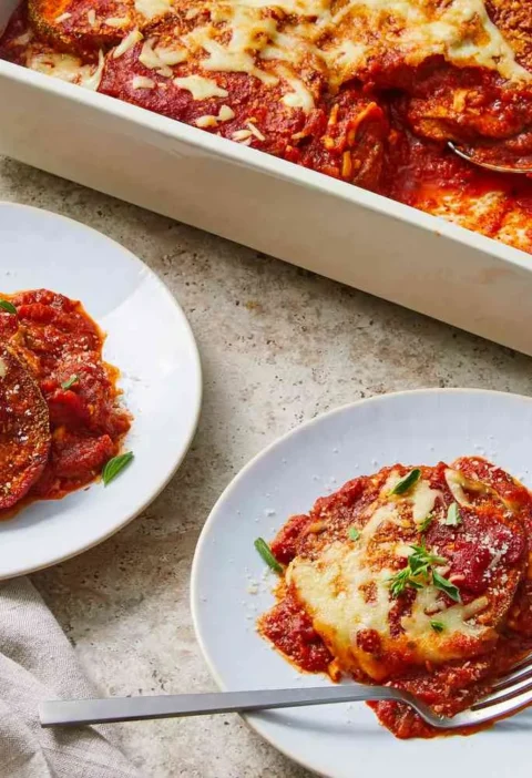 Martha Stewart baked eggplant parmesan in a white baking dish and served on two plates with melted mozzarella and fresh herbs