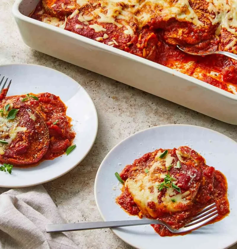 Martha Stewart baked eggplant parmesan in a white baking dish and served on two plates with melted mozzarella and fresh herbs