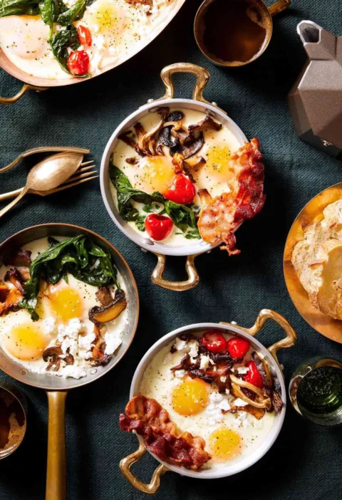 Martha Stewart baked eggs in copper-handled dishes topped with mushrooms, spinach, bacon and Peppadew peppers beside toasted bread