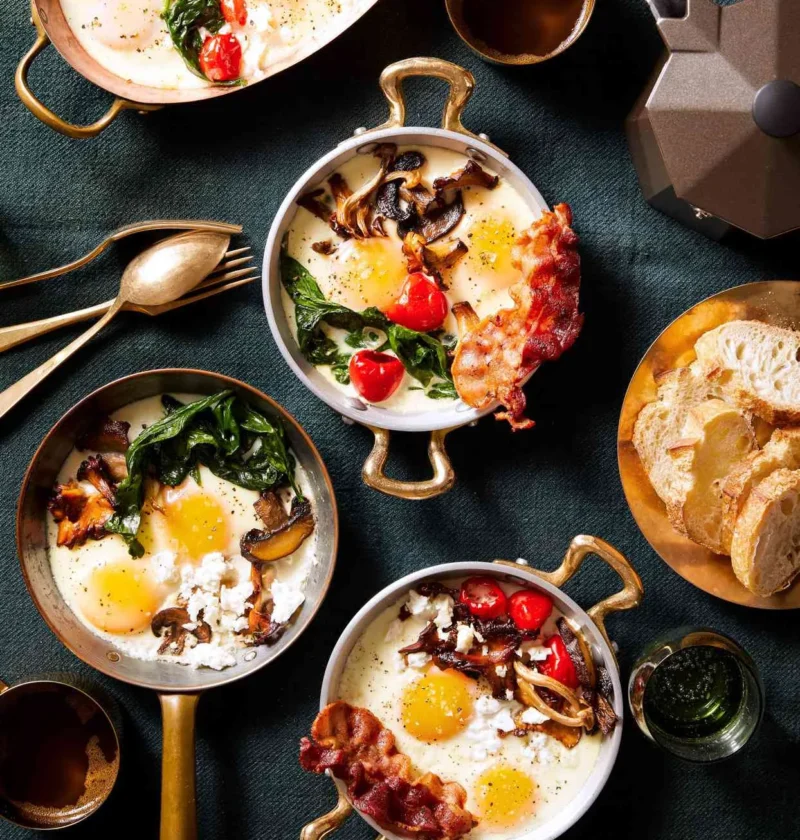 Martha Stewart baked eggs in copper-handled dishes topped with mushrooms, spinach, bacon and Peppadew peppers beside toasted bread