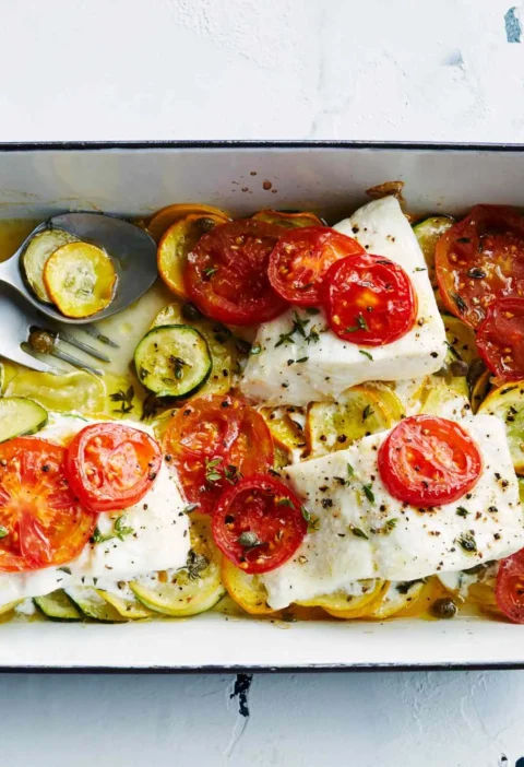 Martha Stewart baked fish with summer squash, white fish fillets topped with sliced tomatoes over yellow and green squash in a baking dish