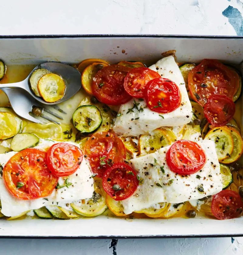 Martha Stewart baked fish with summer squash, white fish fillets topped with sliced tomatoes over yellow and green squash in a baking dish
