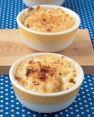 Martha Stewart baked macaroni and cheese in two yellow-banded ramekins with a golden breadcrumb topping on a wooden board