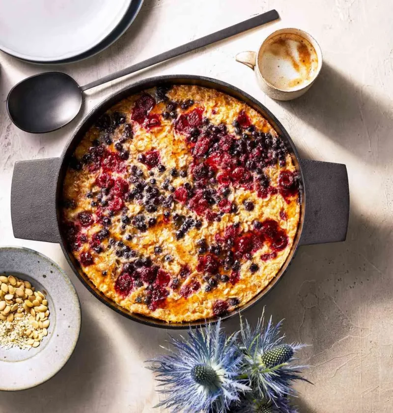Martha Stewart baked oatmeal for a crowd with berries and seeds in a black baking dish with pepitas on the side