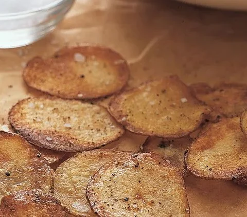 Martha Stewart baked potato chips, golden and crisp, scattered on parchment paper next to a small bowl of coarse salt