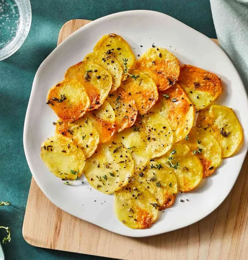 Martha Stewart baked potato slices, golden and crispy, with thyme leaves on a white plate
