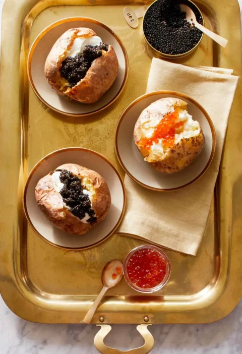Martha Stewart baked potatoes with crème fraîche and caviar served on a gold tray with salmon roe in a small bowl