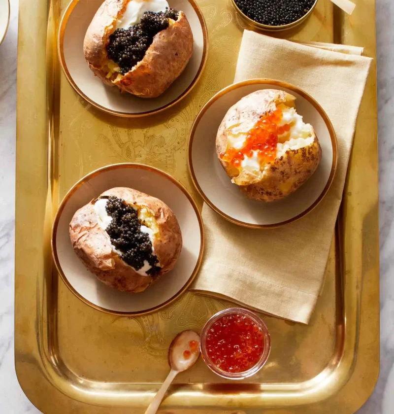 Martha Stewart baked potatoes with crème fraîche and caviar served on a gold tray with salmon roe in a small bowl