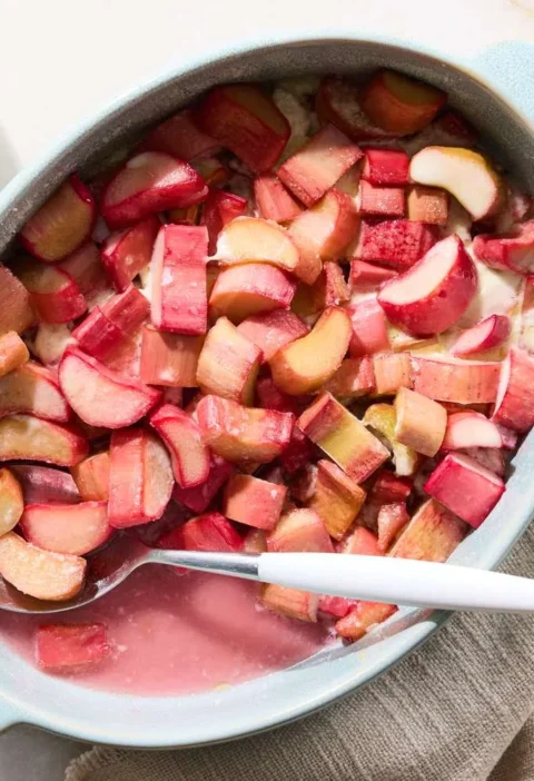 Martha Stewart baked rhubarb in a light blue oval baking dish with a white spoon, with a small bowl of rhubarb nearby
