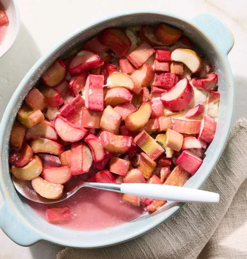 Martha Stewart baked rhubarb in a light blue oval baking dish with a white spoon, with a small bowl of rhubarb nearby