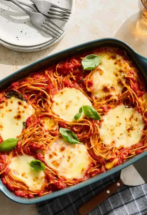 Martha Stewart baked spaghetti and mozzarella in a teal baking dish topped with melted cheese and fresh basil leaves