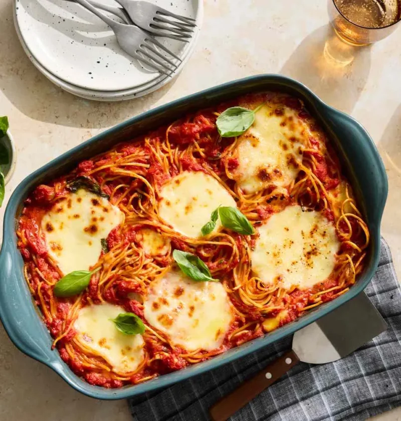 Martha Stewart baked spaghetti and mozzarella in a teal baking dish topped with melted cheese and fresh basil leaves