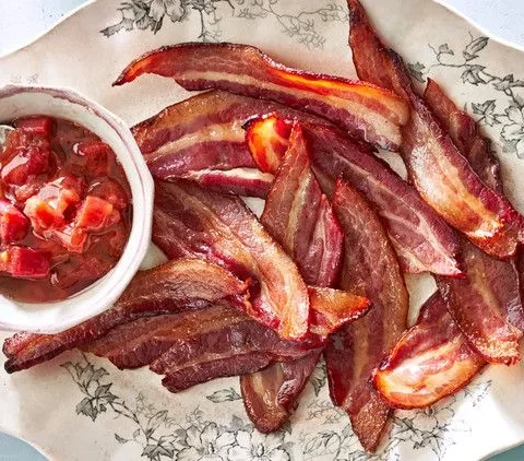 Martha Stewart baked thick-cut bacon with rhubarb chutney on a floral platter with a small bowl of chunky chutney and a spoon