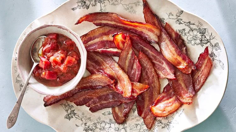 Martha Stewart baked thick-cut bacon with rhubarb chutney on a floral platter with a small bowl of chunky chutney and a spoon