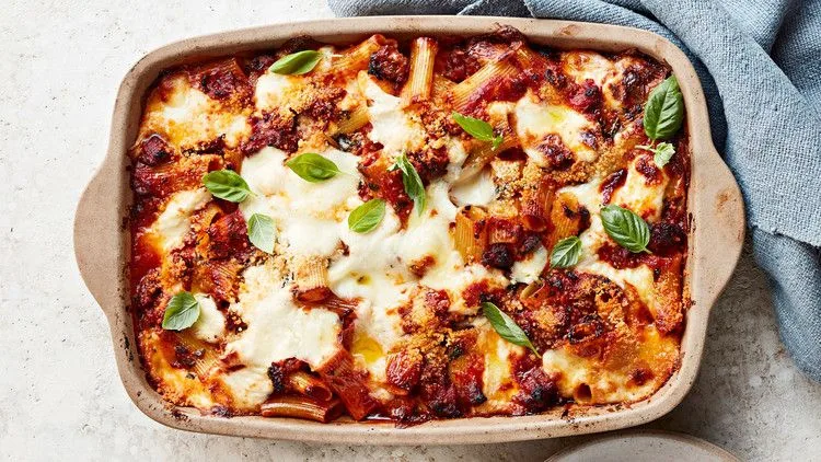 Martha Stewart baked ziti with sausage and bechamel in a baking dish topped with melted mozzarella and fresh basil leaves