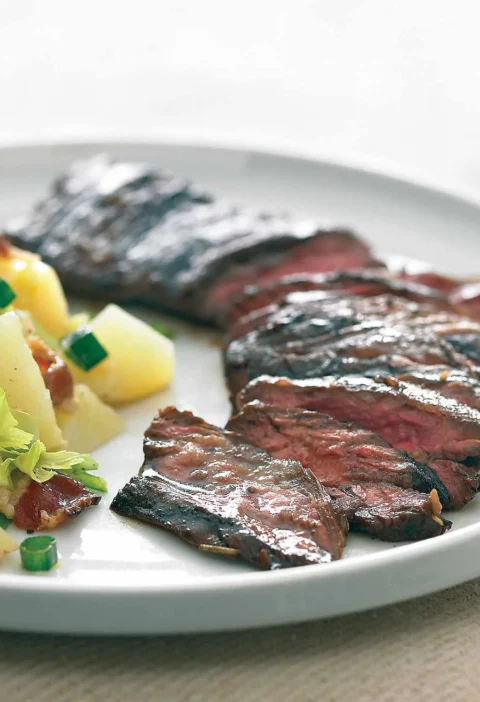 Sliced balsamic marinated skirt steak served on a white plate with potato salad and green onions