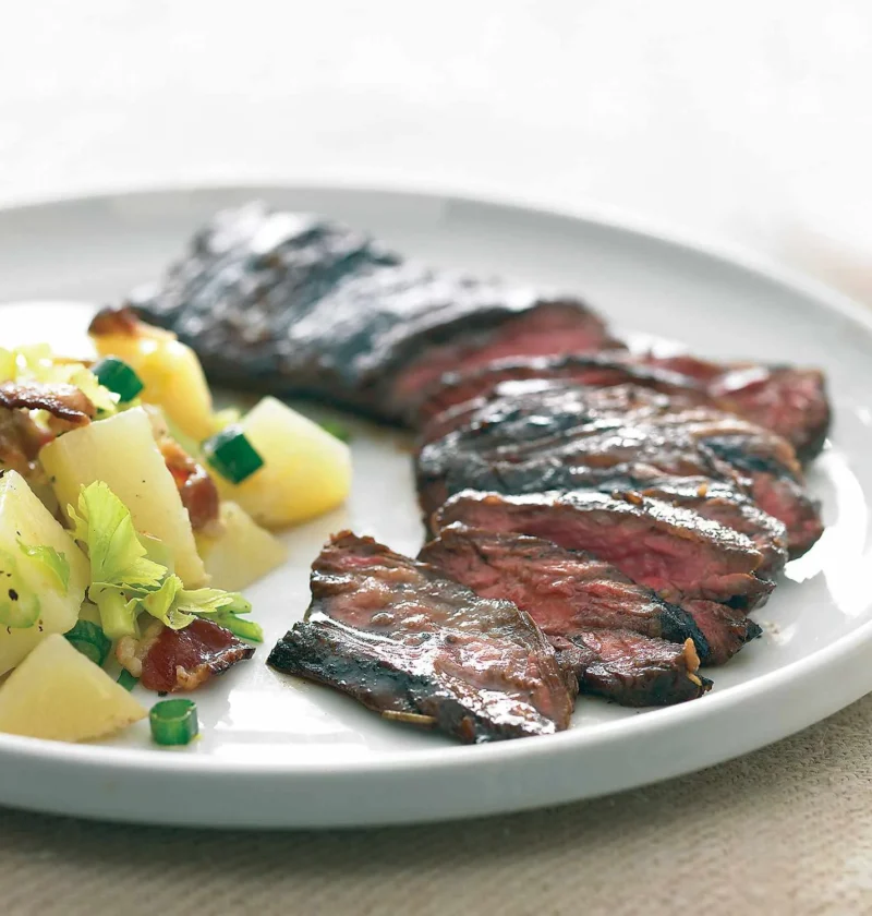 Sliced balsamic marinated skirt steak served on a white plate with potato salad and green onions