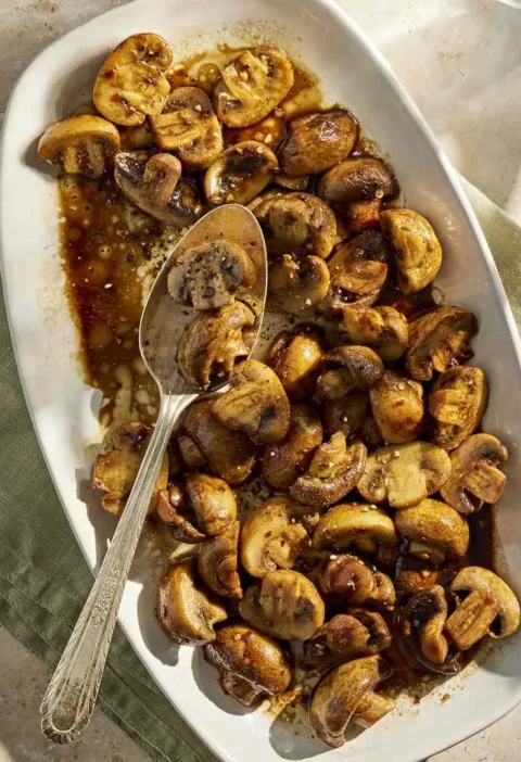 Martha Stewart balsamic mushrooms glazed golden brown on an oval white serving platter with a spoon