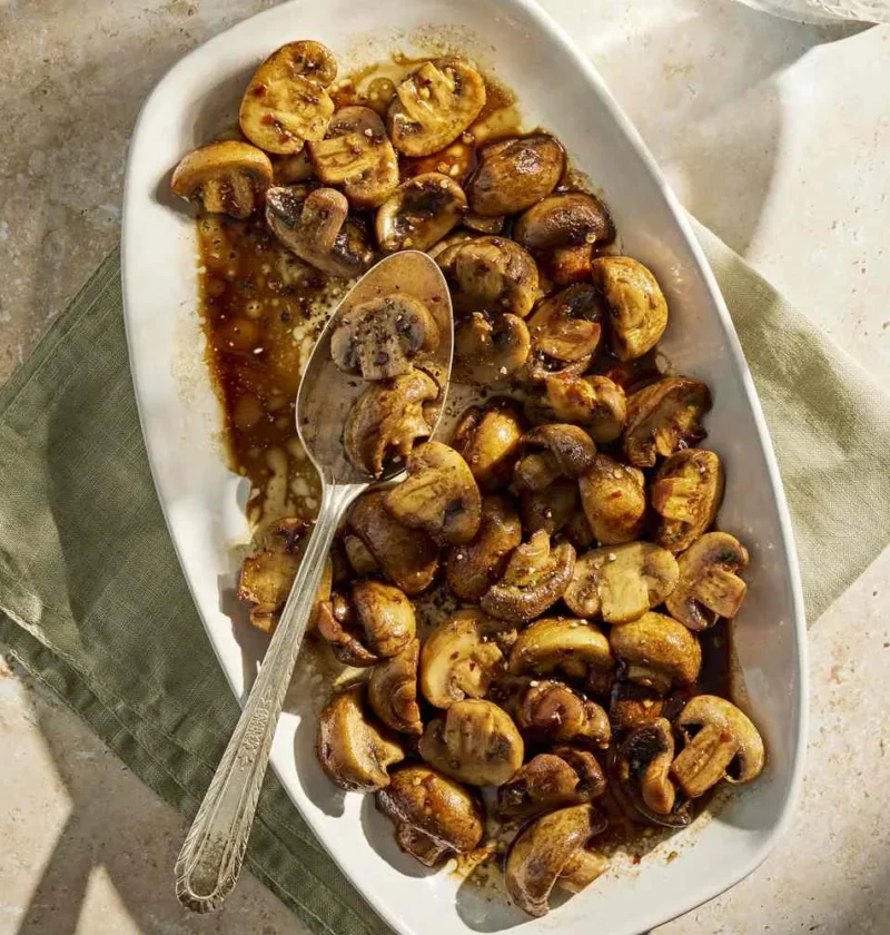 Martha Stewart balsamic mushrooms glazed golden brown on an oval white serving platter with a spoon