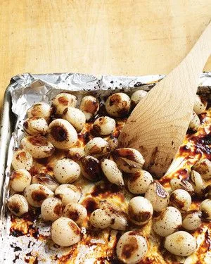 Martha Stewart balsamic-roasted pearl onions on a foil-lined baking sheet with a wooden spoon, glazed and browned