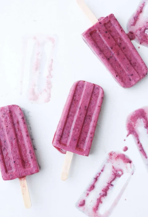 Martha Stewart banana, berry and buttermilk popsicles in pink-purple on a white surface with wooden sticks
