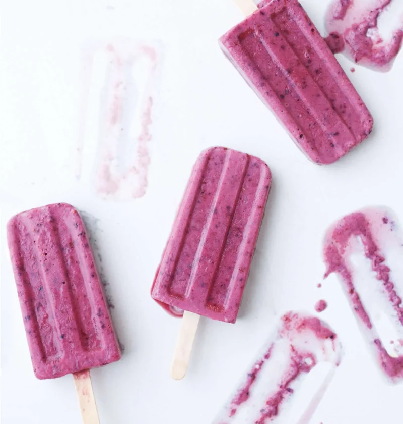 Martha Stewart banana, berry and buttermilk popsicles in pink-purple on a white surface with wooden sticks
