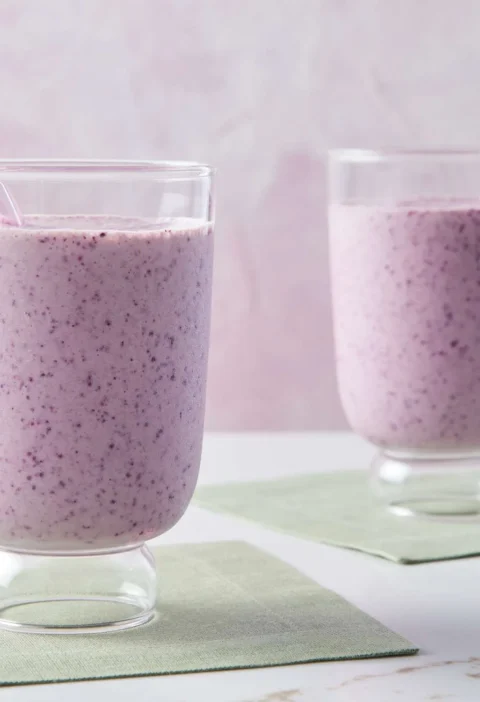 Two glasses of Martha Stewart banana-blueberry smoothie with pink straws on green napkins
