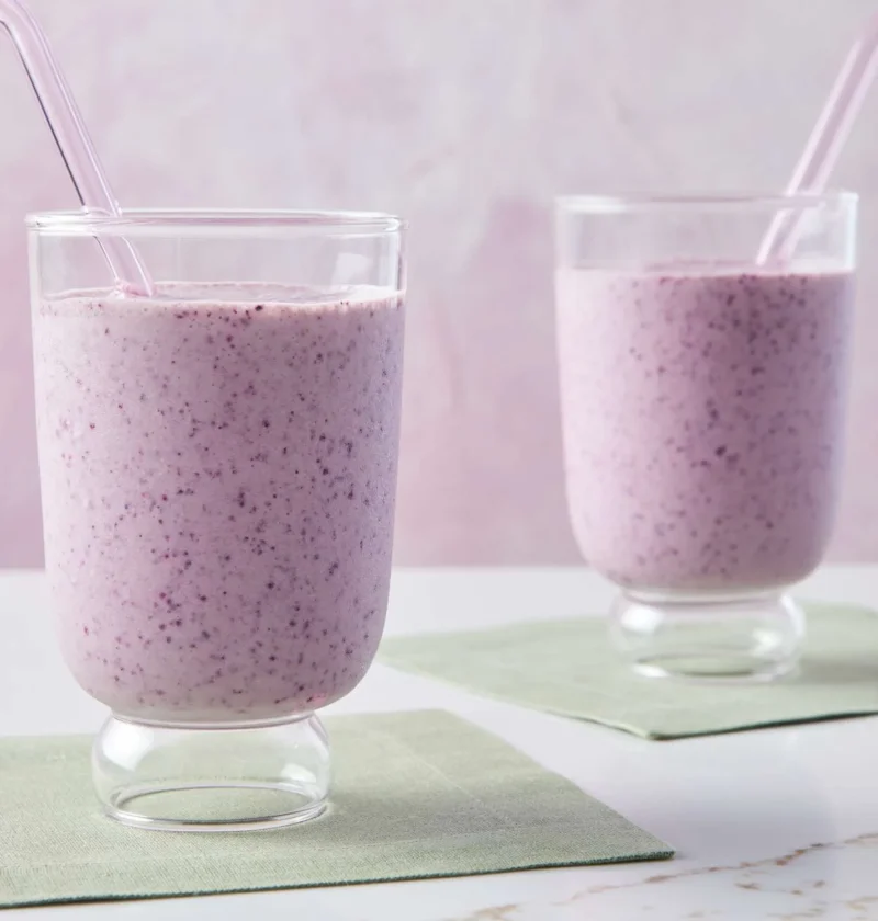 Two glasses of Martha Stewart banana-blueberry smoothie with pink straws on green napkins