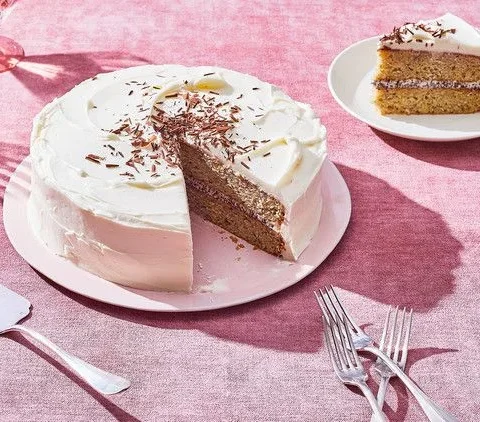 Martha Stewart banana cake with cream-cheese frosting and shaved dark chocolate, with a slice cut out on a pink plate